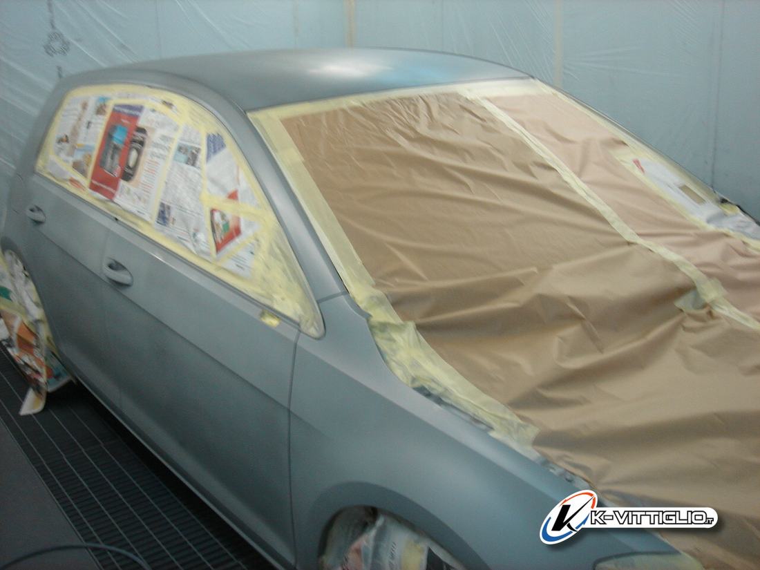 Auto grigia in cabina di verniciatura con vetri e fiancata coperti dalla carta di mascheratura