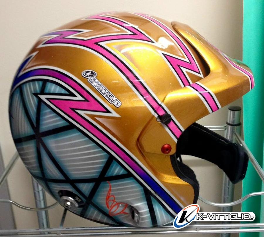 Casco da rally oro con saette fucsia e blu su fondo a rombi