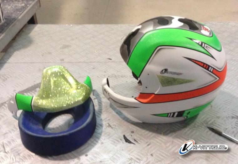 Calotta di un casco da cross verniciata in bianco, verde e rosso accanto alla sua parte interna, sul banco