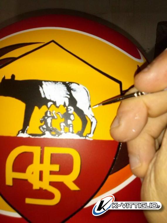 Un pennellino che ripassa a mano i contorni di uno stemma dipinto su un casco